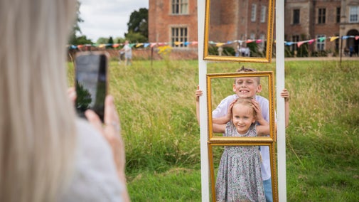 A parent photographs two children as they pose for a photograph while filling an empty picture frame